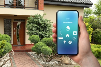 Man using smart home control system via mobile phone near house outdoors, closeup