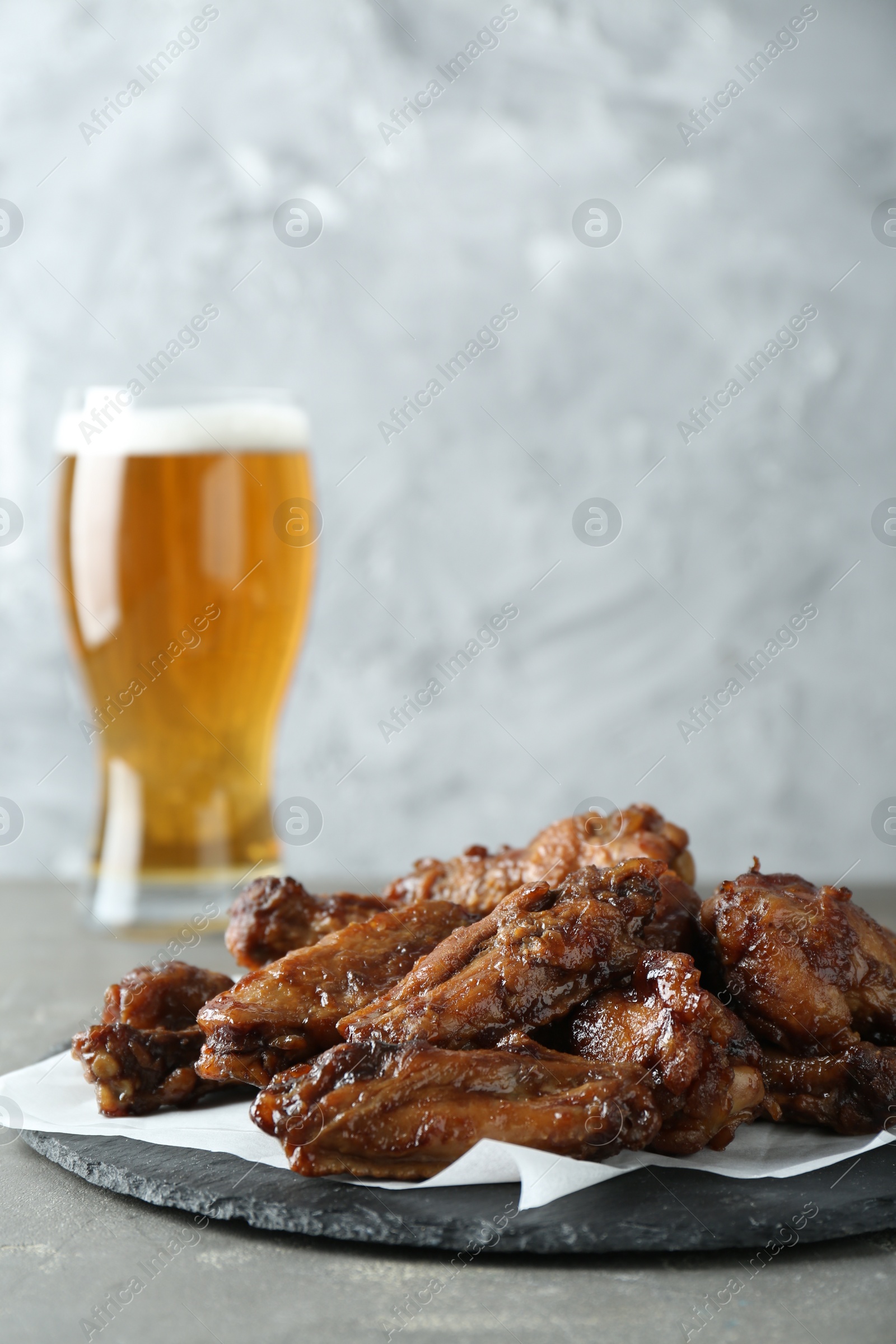 Photo of Delicious chicken wings and glass of beer on grey table, space for text