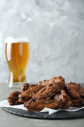 Photo of Delicious chicken wings and glass of beer on grey table, space for text