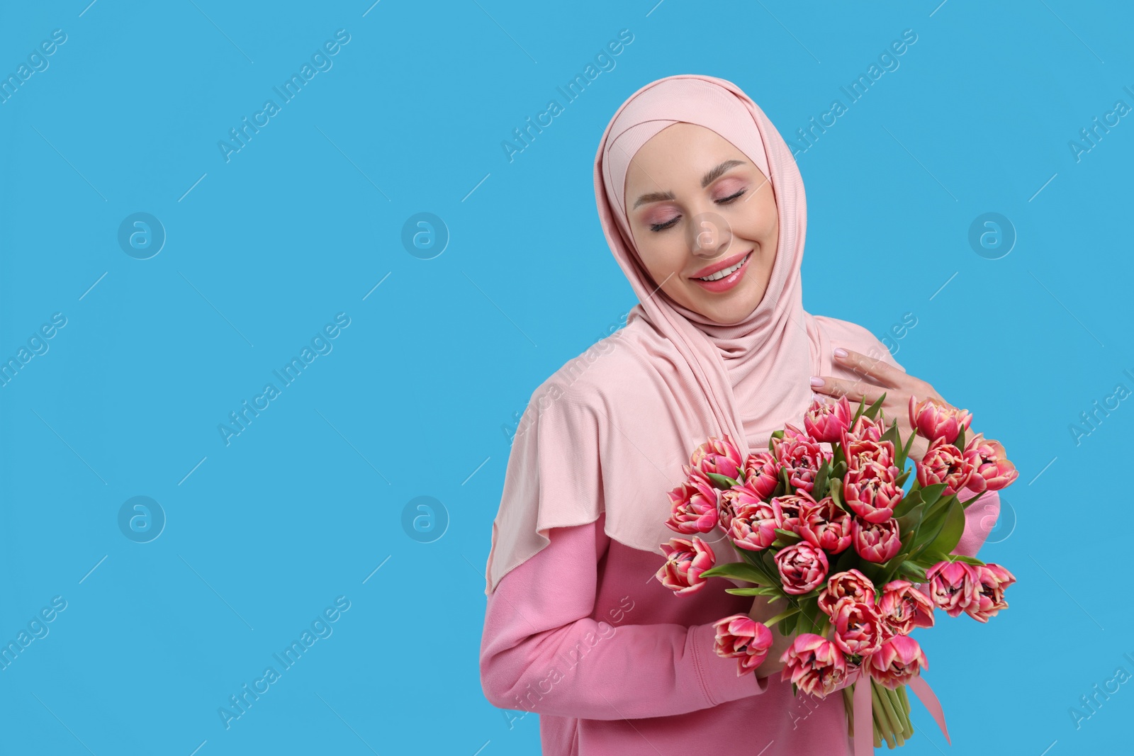 Photo of Happy woman in hijab with beautiful bouquet on light blue background. Space for text