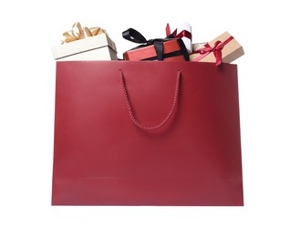 Photo of Dark red paper shopping bag full of gift boxes on white background