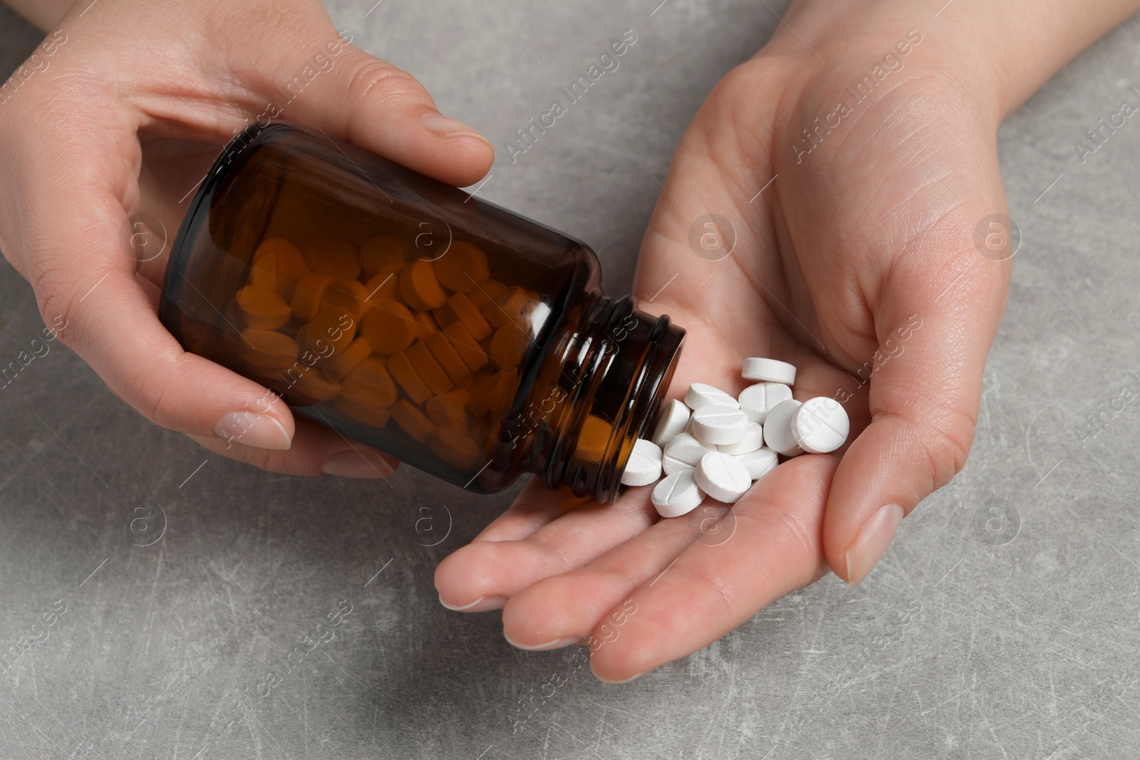 Photo of Woman pouring pills from bottle onto hand at light grey table, closeup