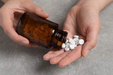 Woman pouring pills from bottle onto hand at light grey table, closeup