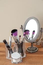 Organizer with cosmetic products for makeup and mirror on table against light wall