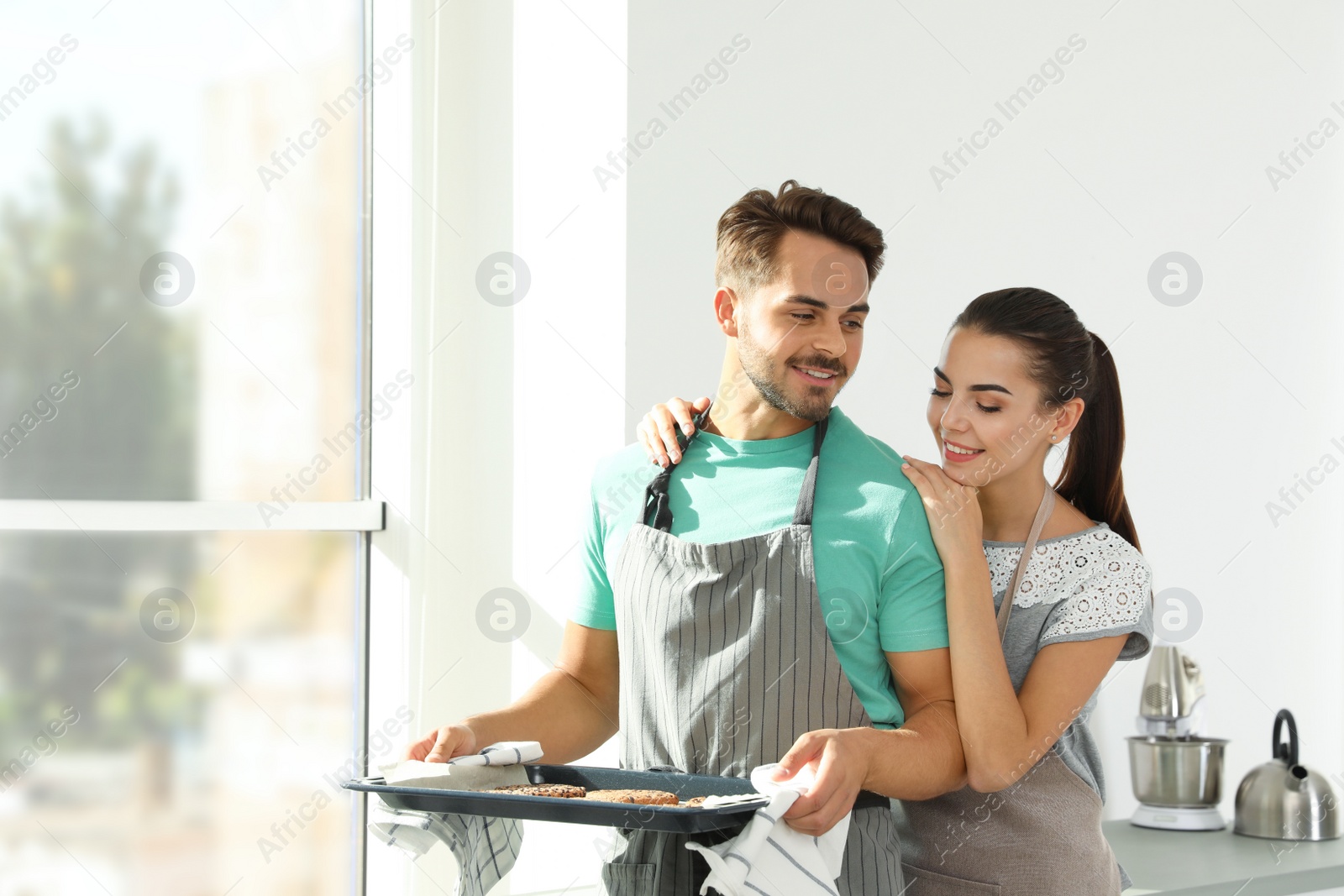 Photo of Young couple with oven sheet of homemade cookies in kitchen, space for text