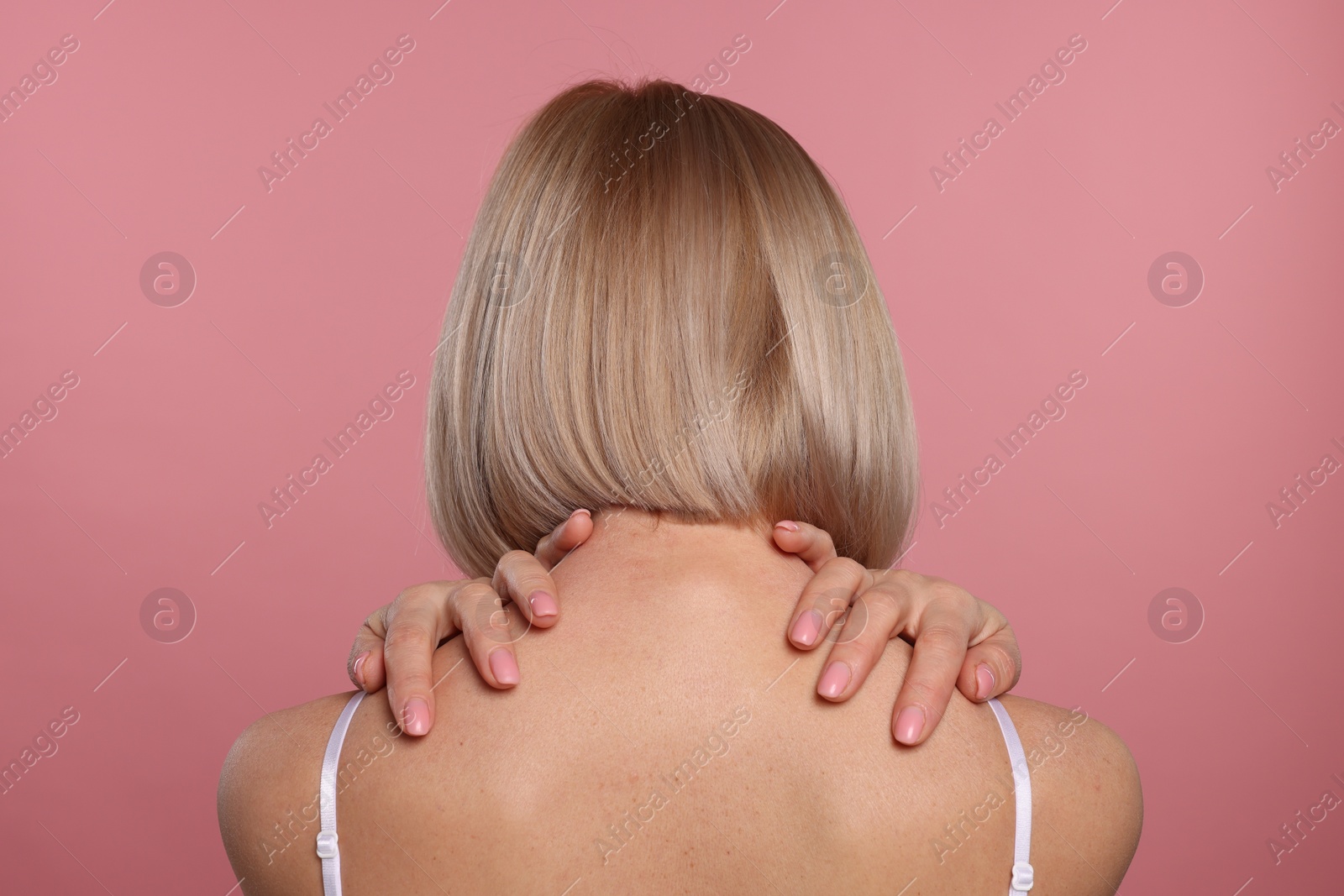 Photo of Woman suffering from pain in her neck on pink background, back view