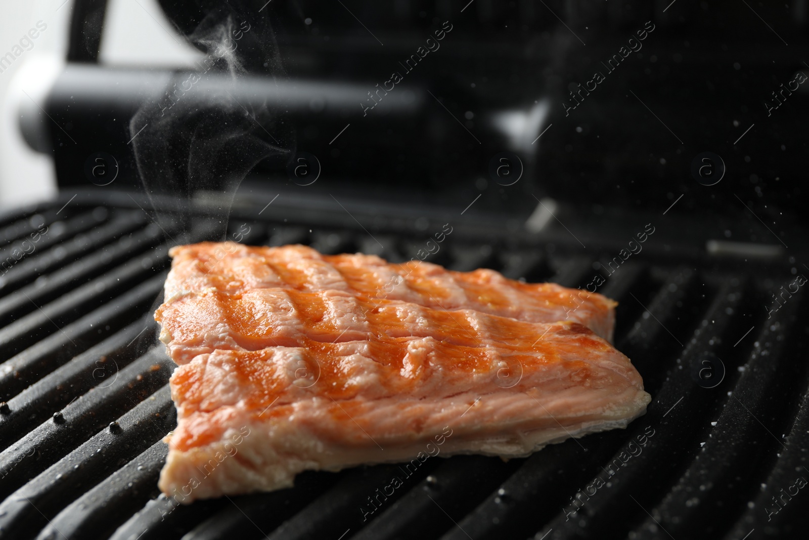 Photo of Tasty salmon cooking on electric grill, closeup