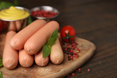 Photo of Delicious boiled sausages, basil and peppercorns on wooden table, closeup