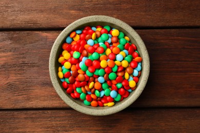 Bowl with tasty colorful candies on wooden table, top view