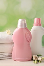 Bottles of laundry detergents, clean clothes and roses on white wooden table