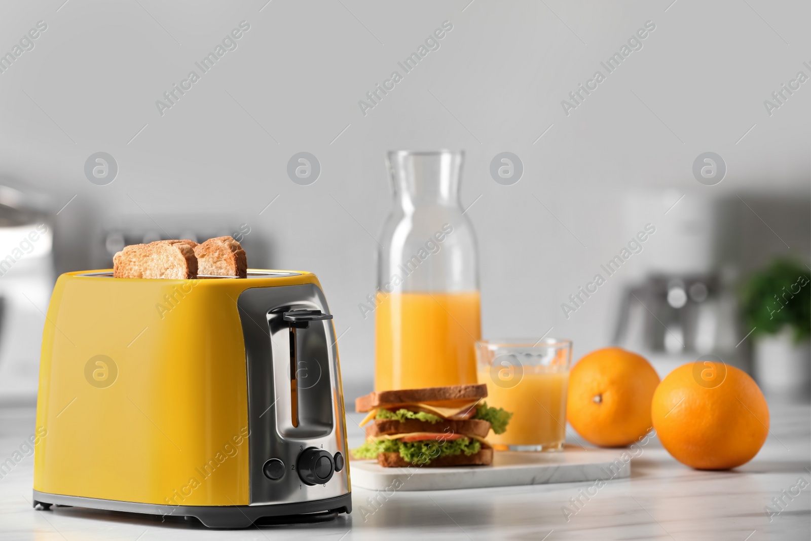 Photo of Yellow toaster with roasted bread slices, sandwich, oranges and juice on white marble table