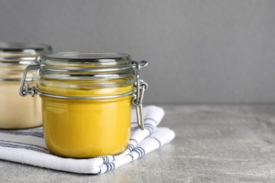 Photo of Jars with mayonnaise and mustard on light grey table, closeup. Space for text