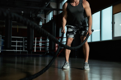 Photo of Man working out with battle ropes in modern gym, closeup