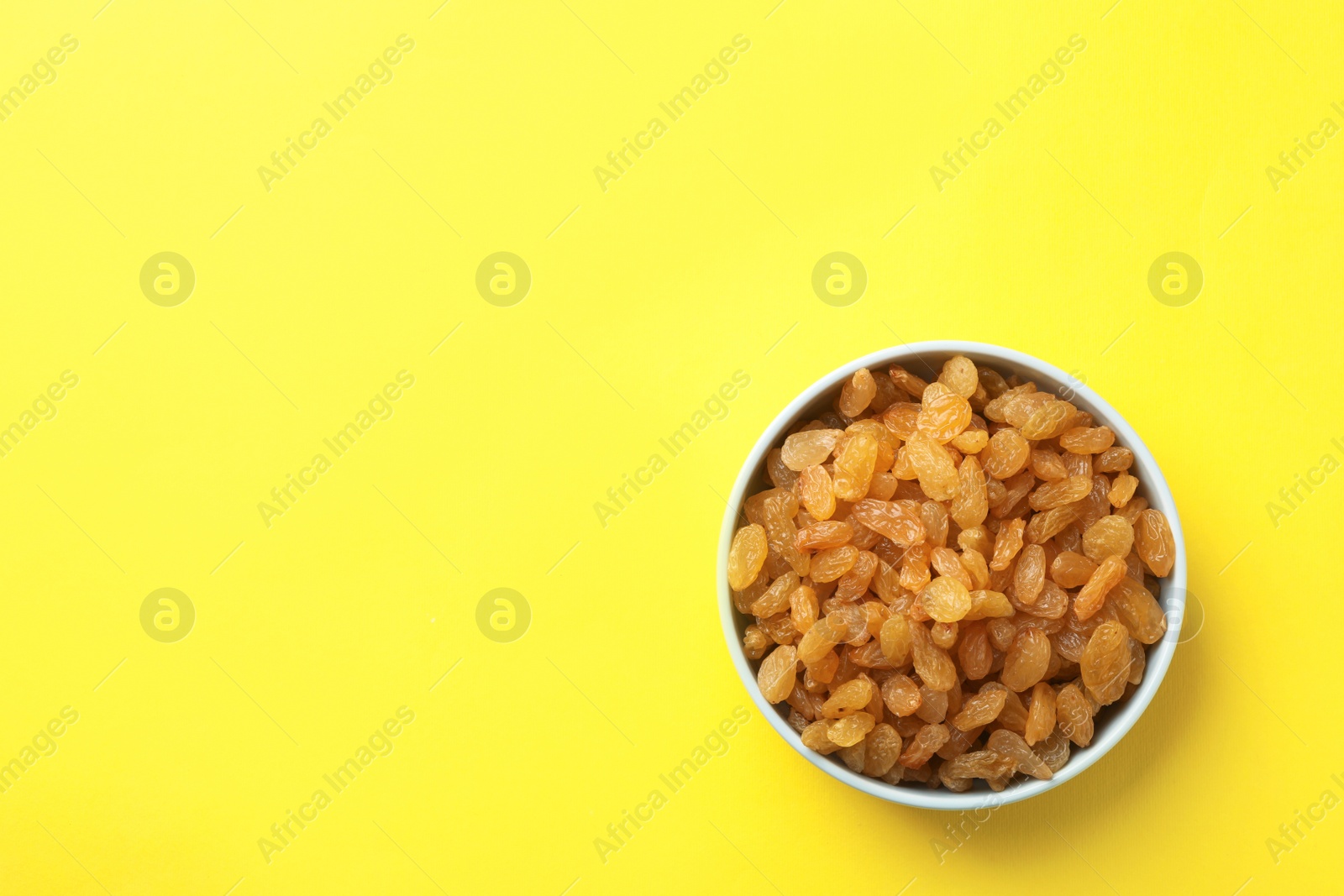 Photo of Bowl with raisins and space for text on color background, top view. Dried fruit as healthy snack