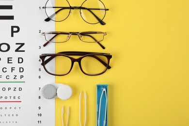 Vision test chart, glasses, lenses and tweezers on yellow background, flat lay. Space for text