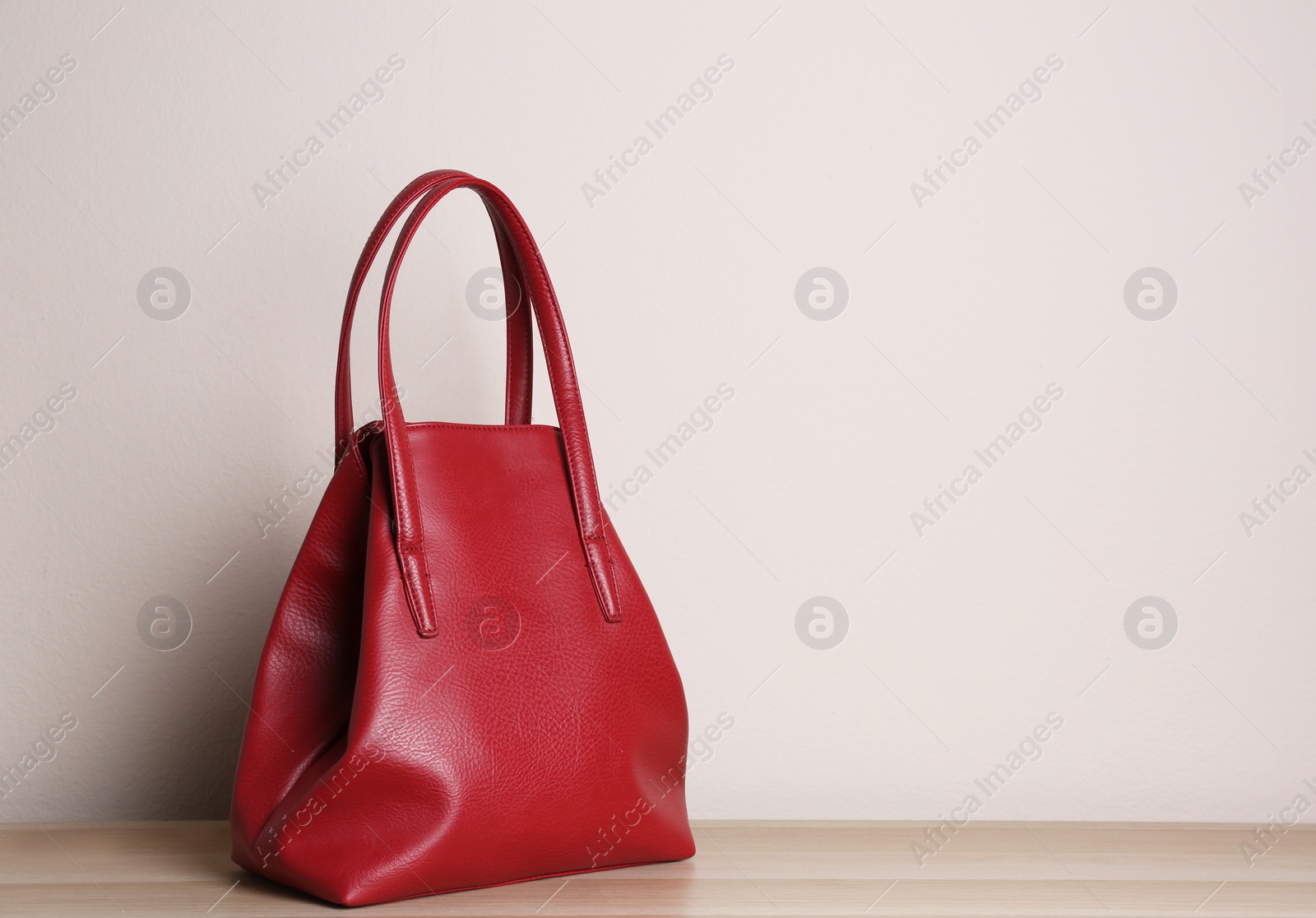 Photo of Stylish red woman's bag on wooden table. Space for text