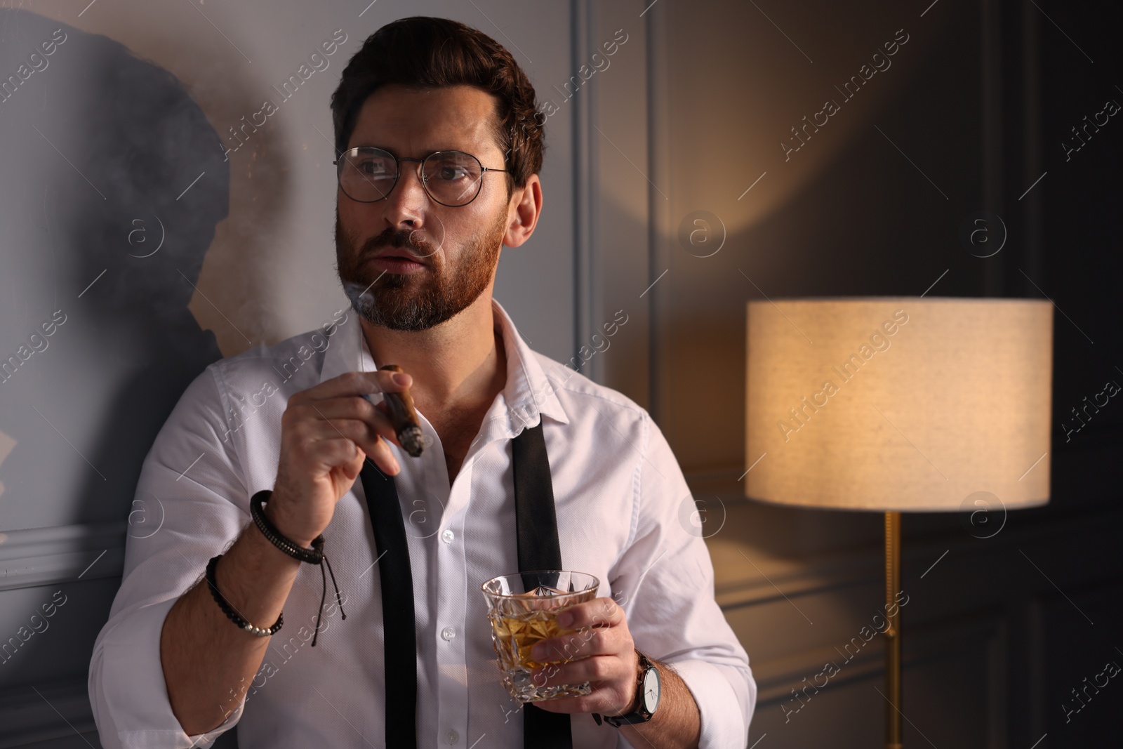 Photo of Thoughtful man with glass of whiskey smoking cigar at home. Space for text
