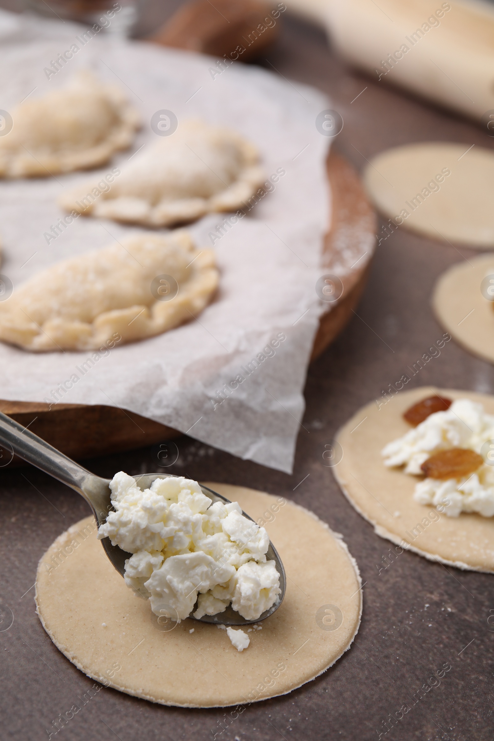 Photo of Process of making dumplings (varenyky) with cottage cheese. Raw dough and ingredients on brown table, closeup