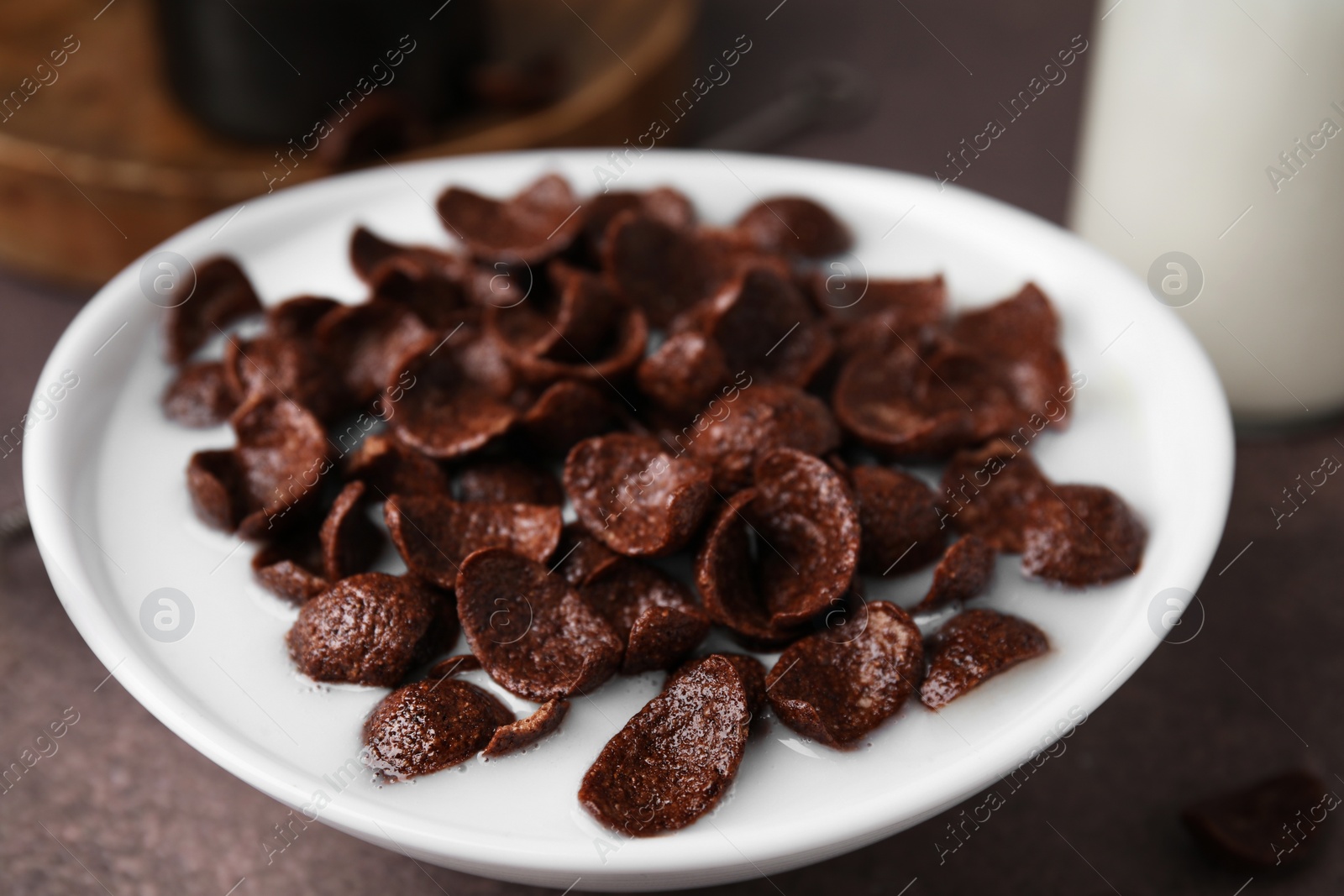 Photo of Breakfast cereal. Chocolate corn flakes and milk in bowl on brown table, closeup