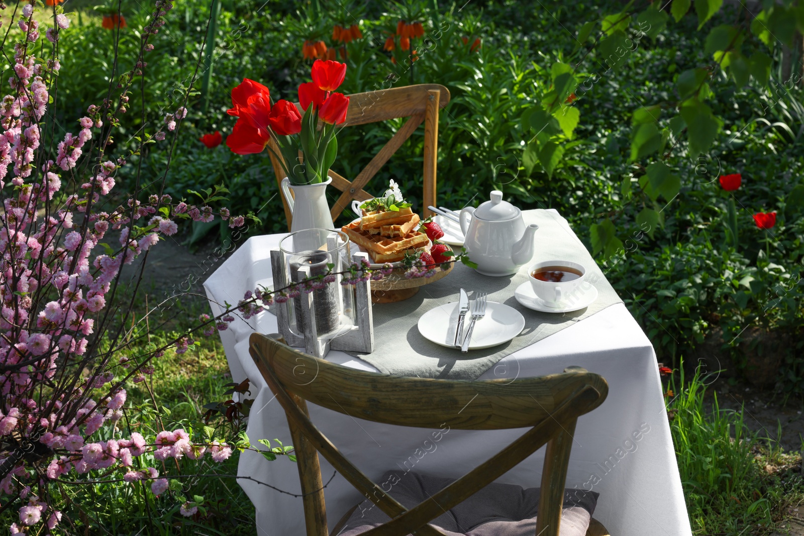 Photo of Beautiful bouquet of tulips and freshly baked waffles on table served for tea drinking in garden