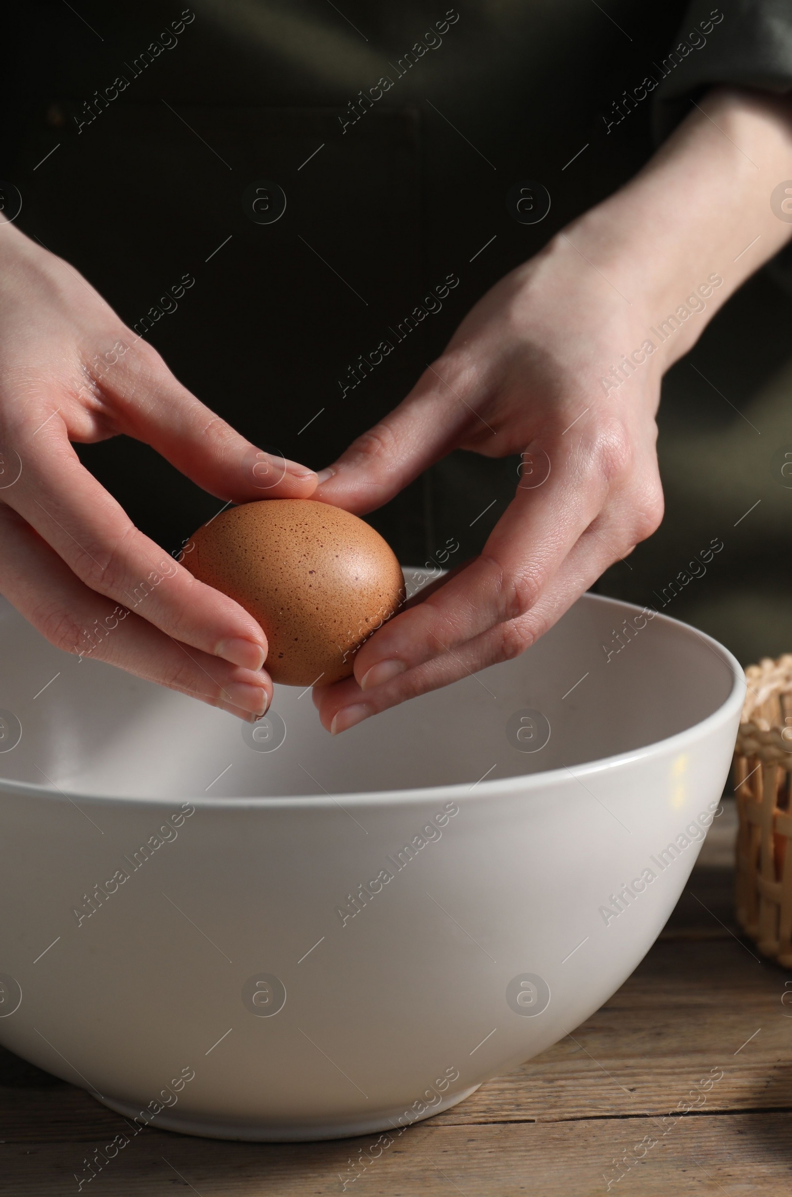 Photo of Making bread. Woman adding egg into dough at wooden table, closeup