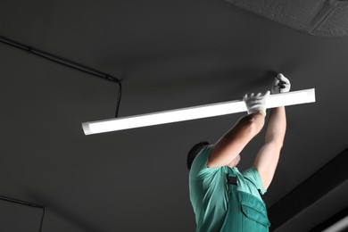 Ceiling light. Electrician installing led linear lamp indoors. Space for text