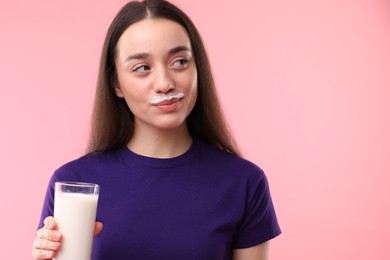 Photo of Cute woman with milk mustache holding glass of tasty dairy drink on pink background. Space for text