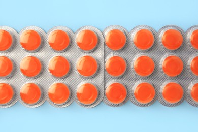 Blisters with orange cough drops on light blue background, flat lay