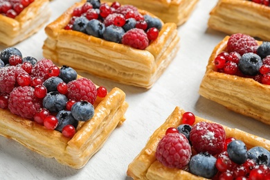 Fresh delicious puff pastry with sweet berries on light table, closeup