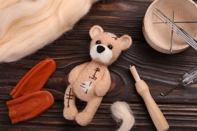 Photo of Felted bear, wool and tools on wooden table, flat lay