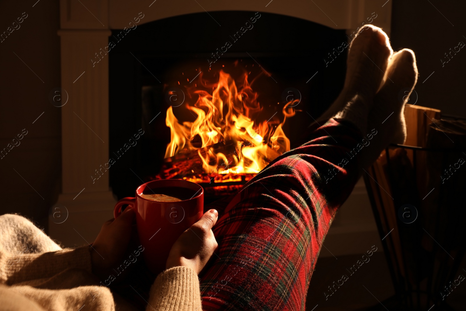 Photo of Woman in knitted socks with cup of drink near fireplace at home, closeup