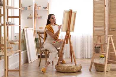 Photo of Beautiful young woman drawing on easel at home