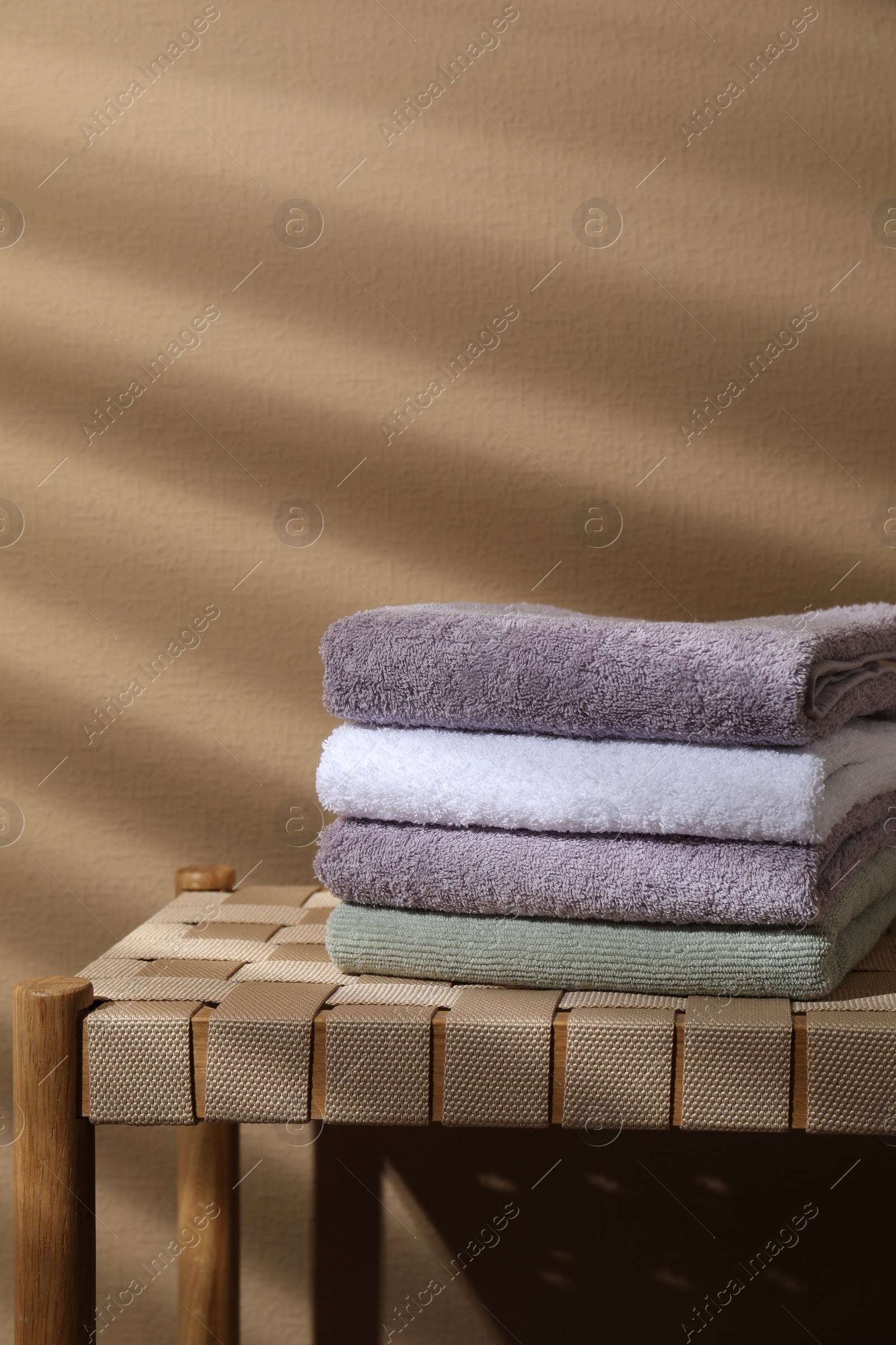 Photo of Stacked terry towels on wicker bench near beige wall