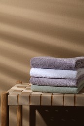 Photo of Stacked terry towels on wicker bench near beige wall