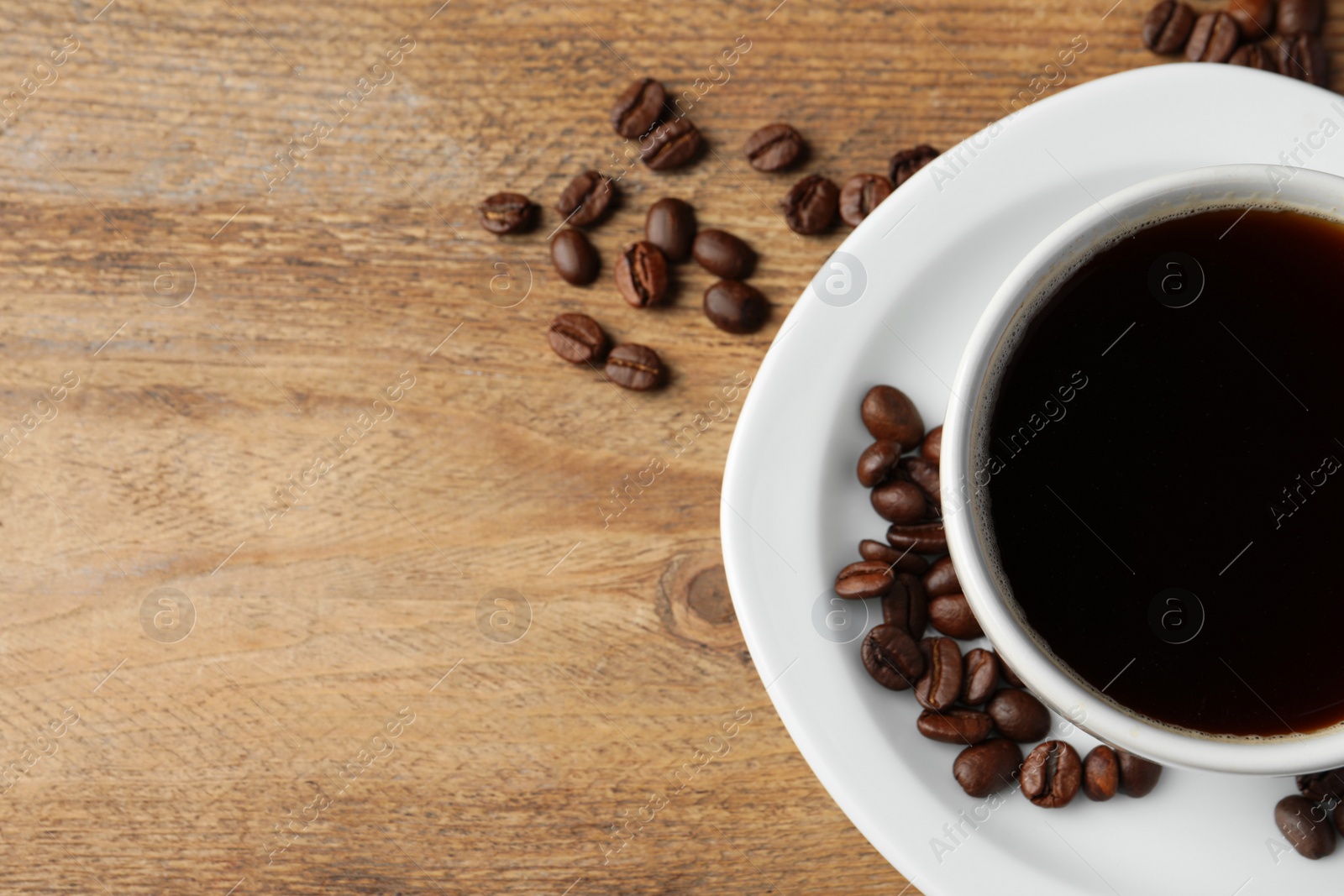 Photo of Cup of hot aromatic coffee and roasted beans on wooden table, flat lay. Space for text