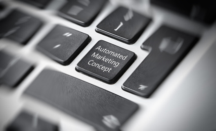 Image of Modern laptop keyboard with text AUTOMATED MARKETING CONCEPT on button, closeup