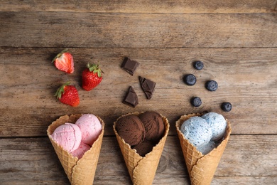Flat lay composition with delicious ice creams in waffle cones on wooden table