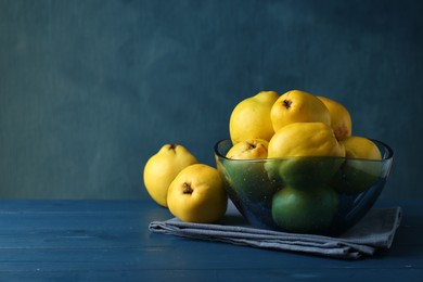 Photo of Tasty ripe quinces in bowl on blue wooden table, space for text