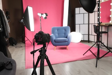 Photo of Stylish blue armchair in photo studio with professional equipment, focus on camera