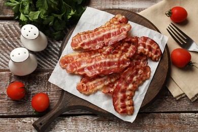 Photo of Fried bacon slices, tomatoes, parsley and spices on wooden rustic table, flat lay