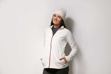 Photo of Woman wearing fleece jacket and hat on light grey background. Winter sport clothes