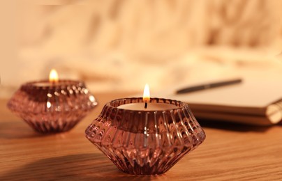 Burning candles in beautiful glass holders on wooden table indoors, closeup