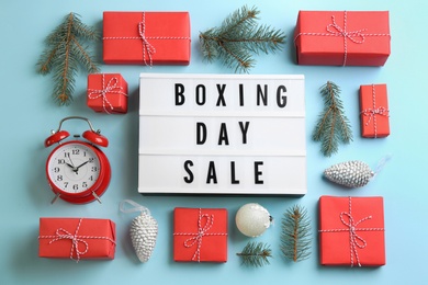 Photo of Lightbox with phrase BOXING DAY SALE and Christmas decorations on light blue background, flat lay
