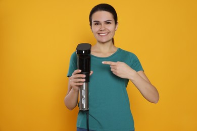 Photo of Beautiful young woman pointing on sous vide cooker against orange background
