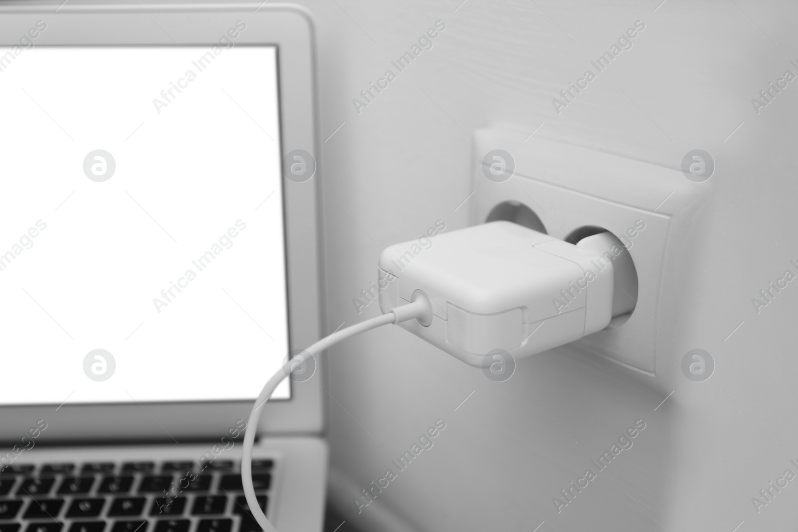 Photo of Modern laptop charging from electric socket indoors, closeup