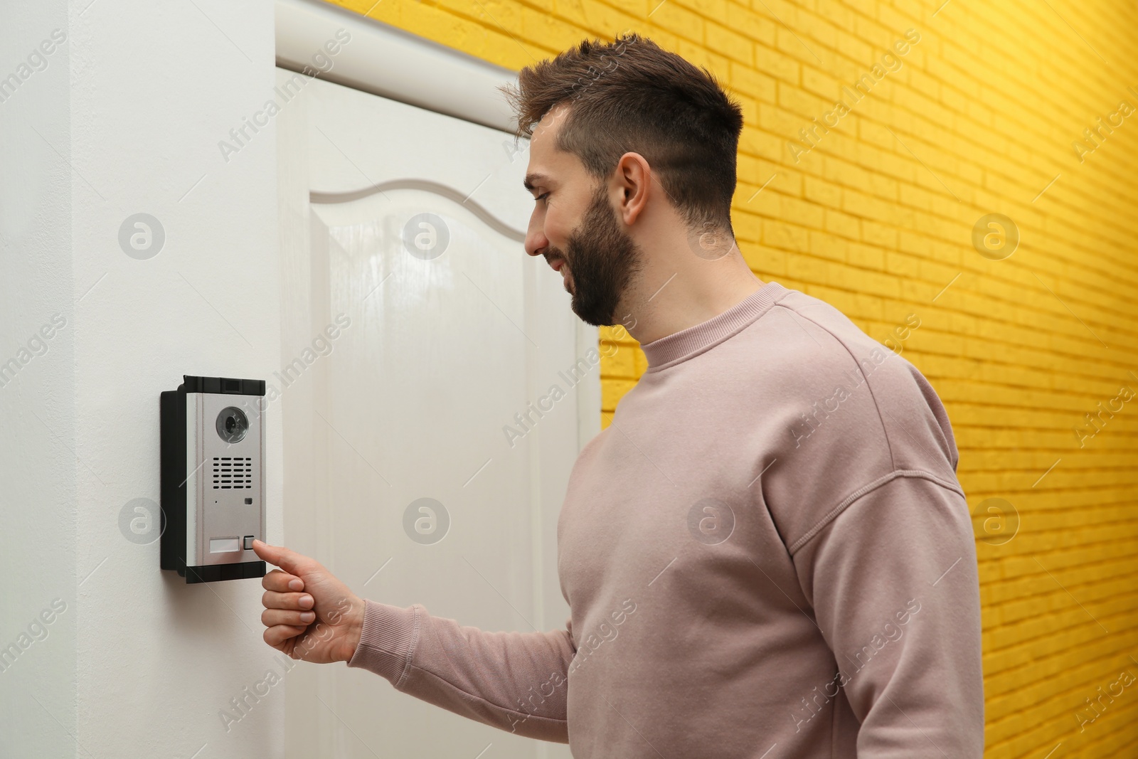 Photo of Happy man ringing intercom with camera in entryway