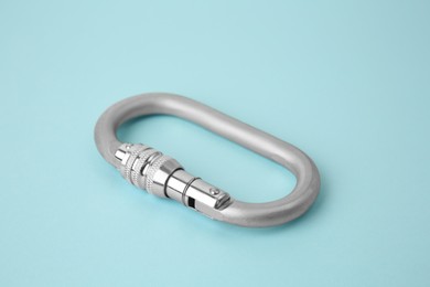 Photo of One metal carabiner on light blue background, closeup