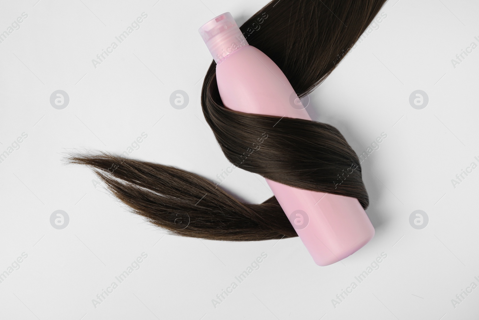 Photo of Shampoo bottle wrapped in lock of hair isolated on white, top view. Natural cosmetic products