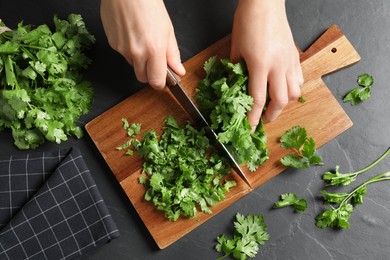 Photo of Woman cutting fresh green cilantro at black table, top view