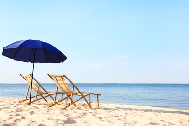 Empty wooden sunbeds and umbrella on sandy shore. Beach accessories